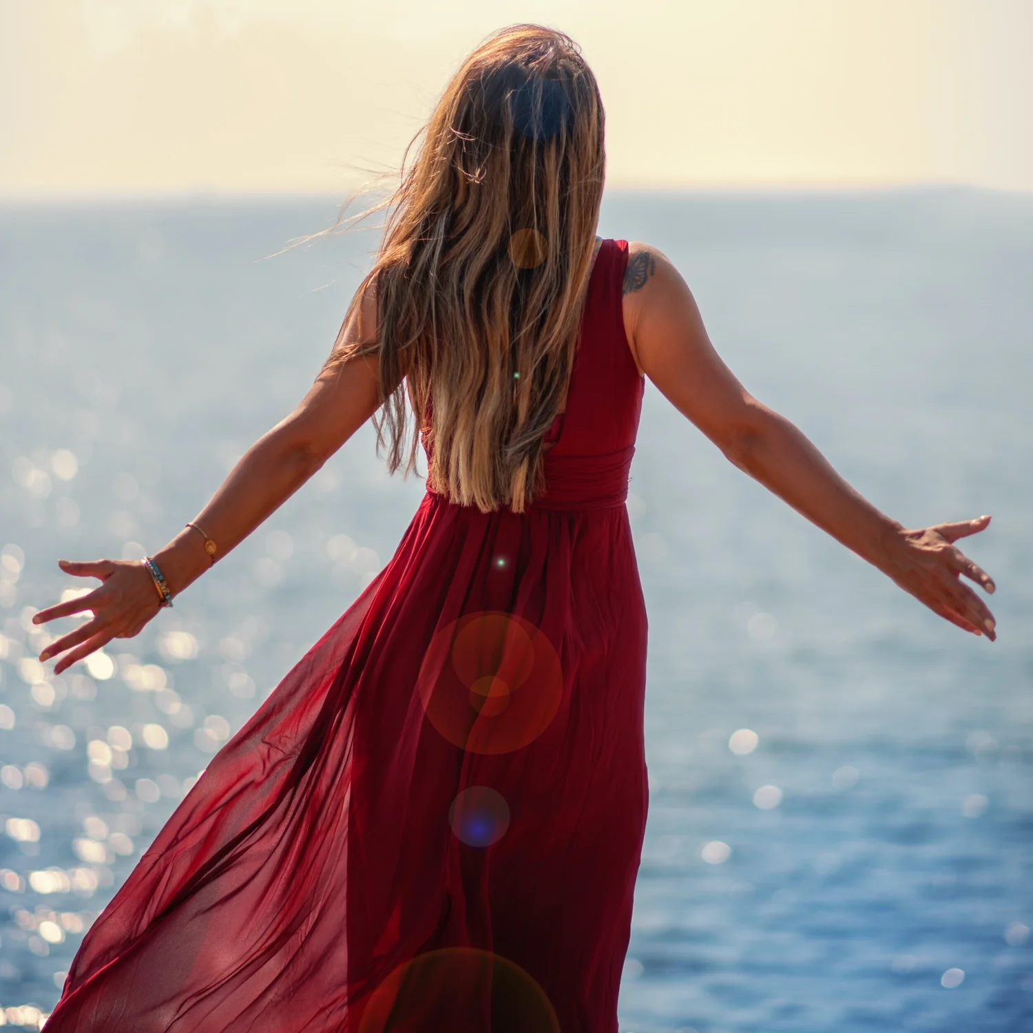 Woman in a flowing rust-red dress facing the ocean in golden light